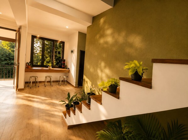 Un interior moderno con una escalera, plantas en macetas y un ventanal con vistas a la vegetación.