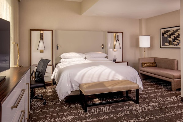 Una habitación de hotel con cama, mesita de noche, lámpara, sillón y sofá.