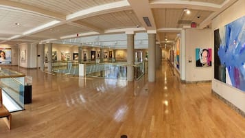 A spacious indoor area with a polished wooden floor, glass railings, and a series of artworks on the walls.
