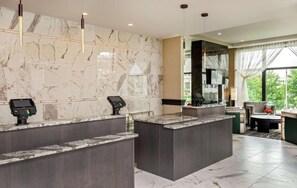 Zona de recepción de hotel con paredes de mármol, dos mostradores y un área de estar con vistas.