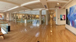 A spacious indoor area with a polished wooden floor, glass railings, and a series of artworks on the walls.