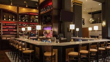 A bar area with a long counter, multiple bar stools, and shelves stocked with bottles.