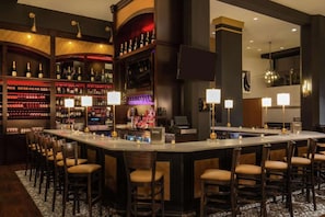 A bar area with a long counter, multiple bar stools, and shelves stocked with bottles.
