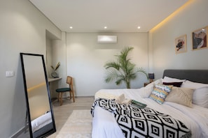 A modern bedroom with a large bed, a desk, a chair, a mirror, and a potted plant. - Delightful stay at Degla by Spacey #39 (Cairo)