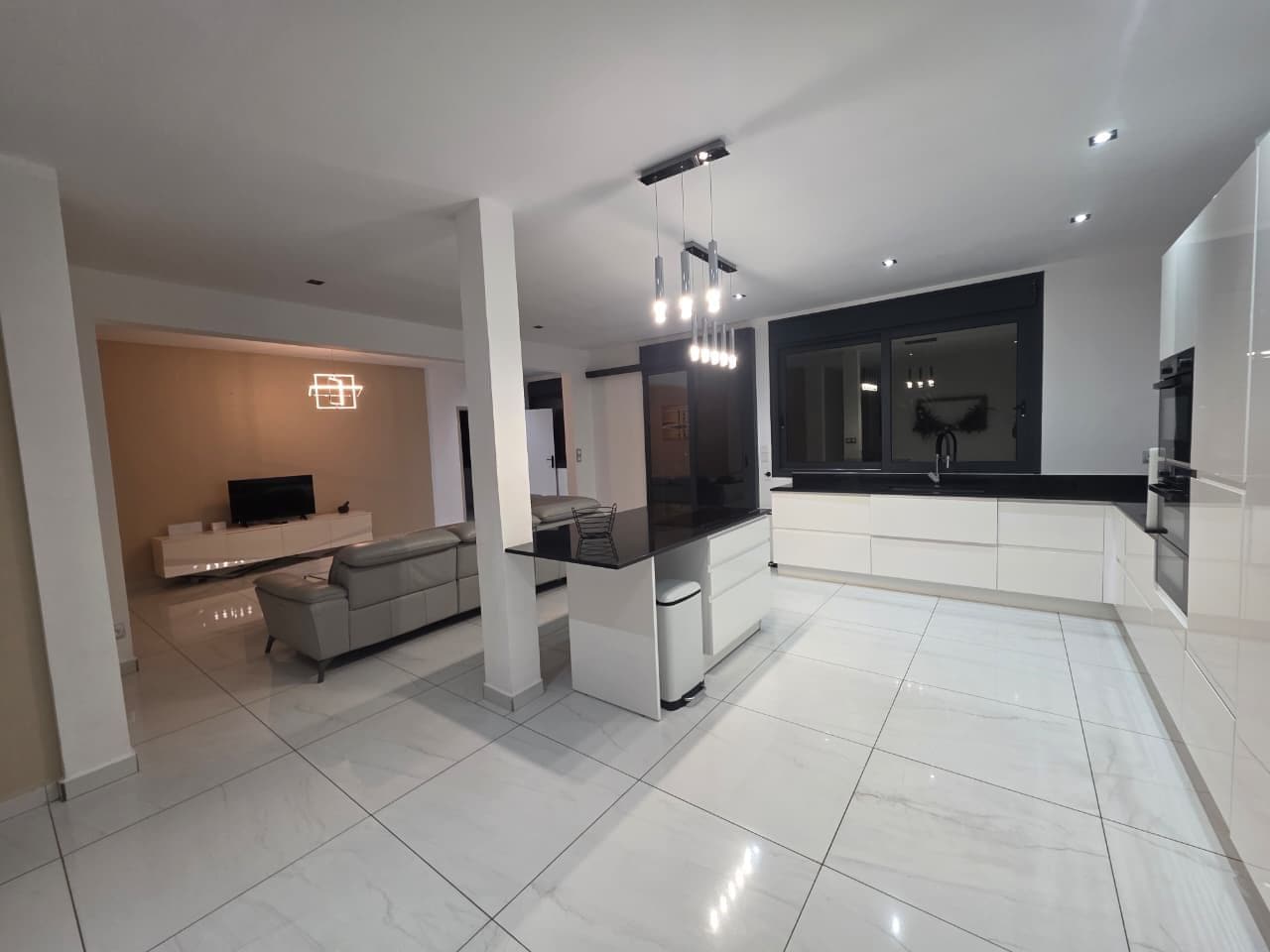 Una cocina moderna con una isla central, una zona de comedor con sofá y un amplio ventanal que proporciona luz natural.