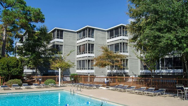 Ein Hotel mit Schwimmbad, Liegestühlen und einer umzäunten Terrassenanlage.