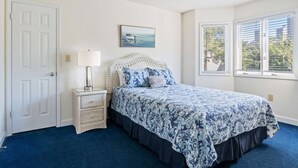 Ein Schlafzimmer mit Bett, Nachttisch, Lampe, einem Gemälde und einem Fenster mit Jalousien.