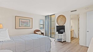 Ein Hotelzimmer mit Bett, Fernseher auf einem Schrank, einem gerahmten Bild an der Wand und Blick auf die Stadt durch das Fenster.