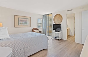 Habitació d'hotel amb un llit, una televisió sobre un suport, un quadre amb marc a la paret i vista a la ciutat per la finestra.