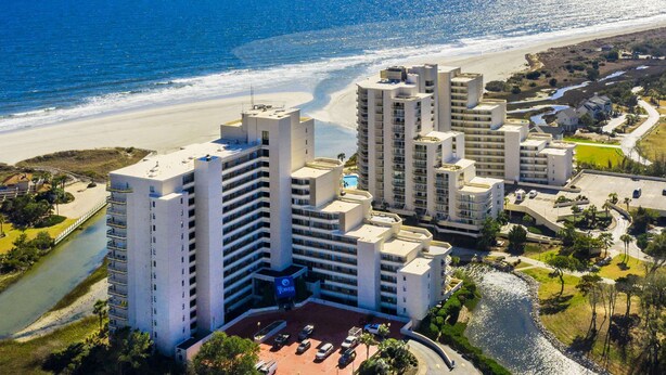 A coastal hotel complex with multiple high-rise buildings, a beachfront, and a river running through the property. - 2BR Oceanfront Condo + On-site Dining, Pools & Gym (Myrtle Beach)