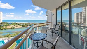 Uma varanda com vista para o oceano, uma piscina e área de refeições com cadeiras e mesa.