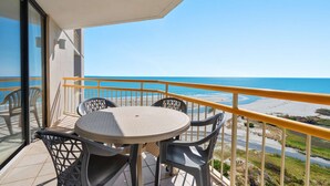 Ein Balkon mit Tisch und Stühlen mit Blick auf Strand und Meer.