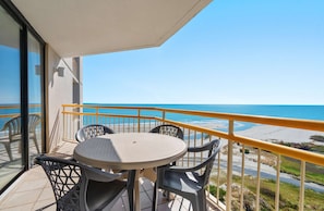 A balcony with a table and chairs, overlooking a beach and ocean. - Spacious 3BR Condo + Beach Access, Kitchen & Pools (Myrtle Beach)