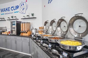 Buffet d'esmorzars amb diverses opcions gastronòmiques i un cartell a la paret que diu 'WAKE-CUP BREAKFAST'.