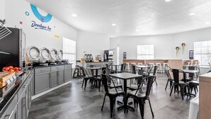 Une cuisine moderne avec un coin repas, dotée d’appareils électroménagers en acier inoxydable, de chaises noires et d’un logo sur le mur.