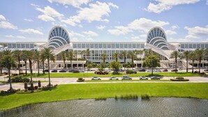 Un bâtiment moderne à l’architecture symétrique, doté d’une cour intérieure avec un élément décoratif aquatique et entouré de palmiers.
