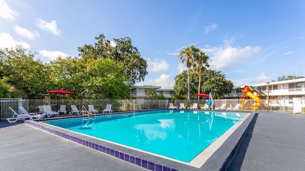 Une piscine rectangulaire dont le bord est recouvert de carreaux, entourée d’une clôture blanche.