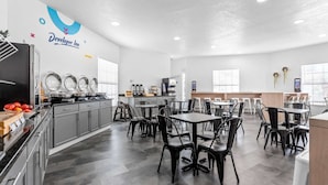 Une cuisine moderne avec un coin repas, dotée d’appareils électroménagers en acier inoxydable, de chaises noires et d’un logo sur le mur.