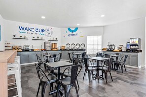 A breakfast area with tables and chairs, a coffee machine, and a wall with logos. - Near Disney World Resort + Free Shuttle. Breakfast (Kissimmee)