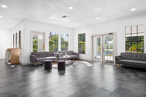 A spacious living area with a modern design, featuring a grey sofa set, a coffee table, and a large window providing a view of the outdoors. - Mins to Disney World Resort + Free Shuttle & Pool (Kissimmee)