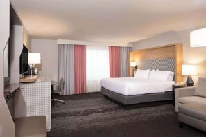 Ein Hotelzimmer mit einem Bett, einem Schreibtisch, einem Sessel, einem Fernseher und einem Fenster mit Vorhängen.