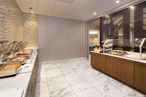 A buffet area with multiple food service stations, a marble-tiled floor, and a glass display case with fruits and beverages. - Stay Near UMD | Wi‑Fi, Pool, and Restaurant (College Park)