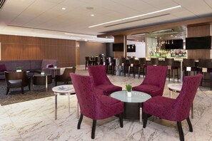 A lobby with a seating area featuring round tables and chairs, a bar area with a counter and bar stools, and a television mounted on the wall. - Stay in College Park | Group‑Friendly. Pool. Bar. (College Park)