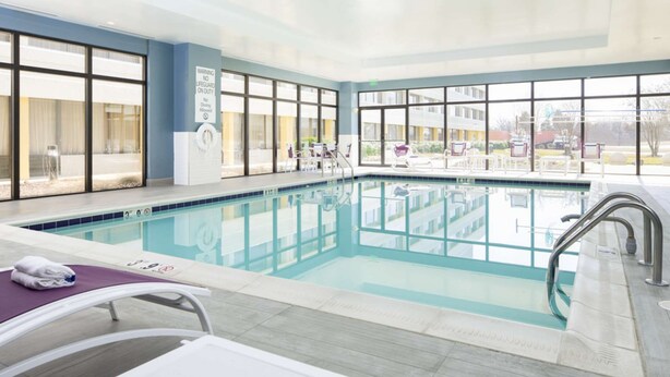 Una piscina interior con paredes de vidrio transparente, una estación de socorristas y sillas de descanso.