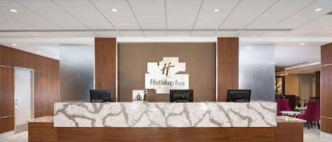 A reception desk with a marble top, two monitors, and a Holiday Inn sign.