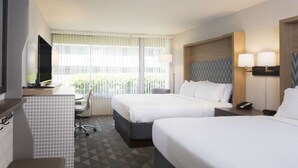Habitación de hotel con dos camas, un escritorio, una silla, un televisor y una ventana con persianas.