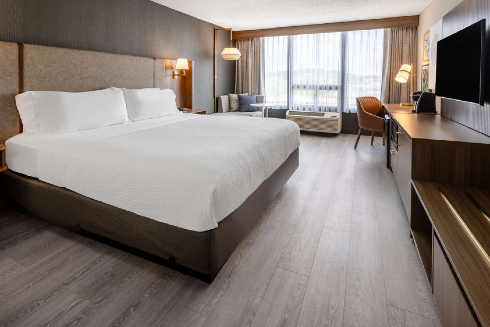 A hotel room with a large bed, a desk, a chair, a flat-screen TV, and a window with curtains.