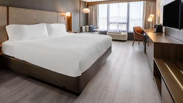 A hotel room with a large bed, a desk, a chair, a flat-screen TV, and a window with curtains.