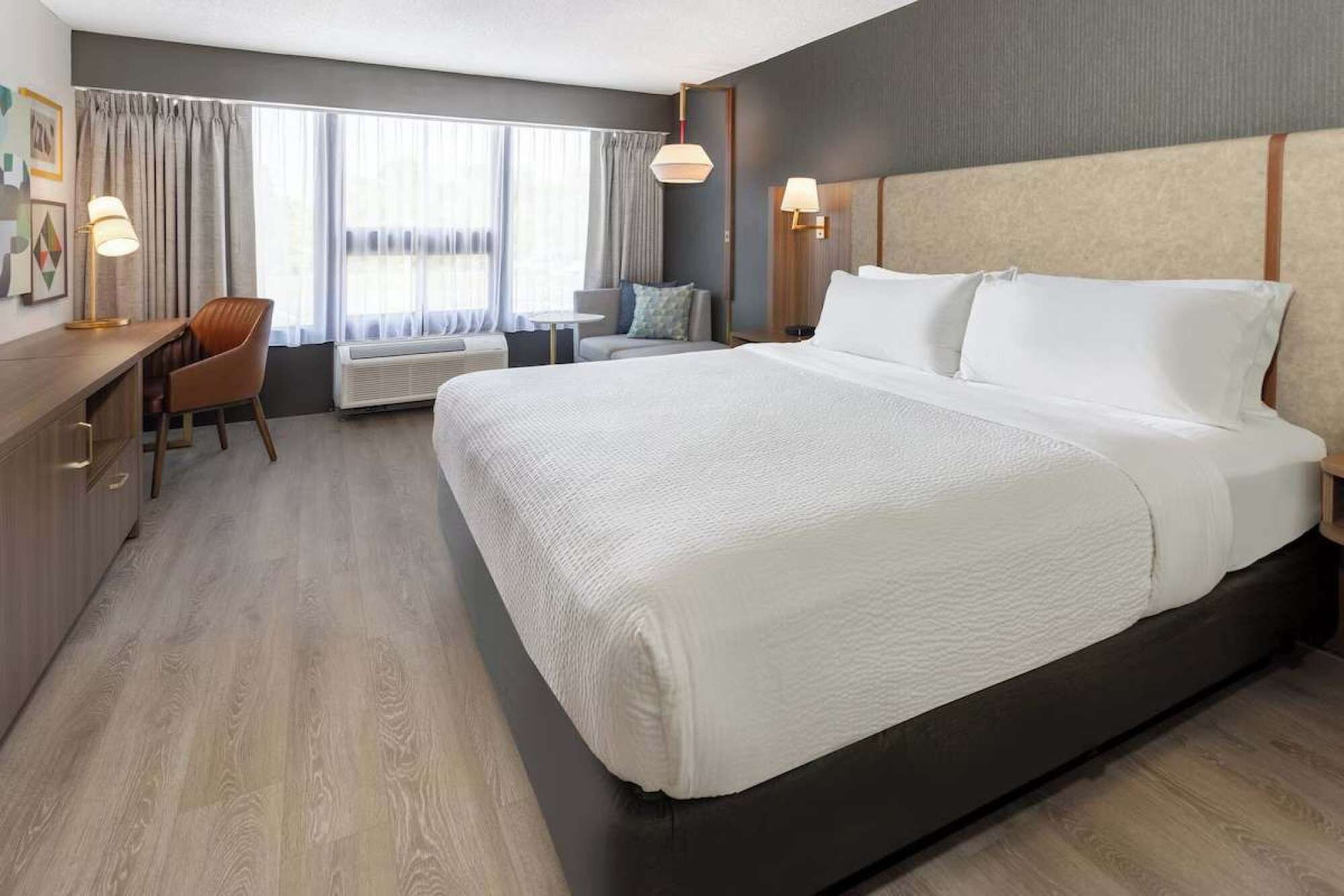 A hotel room with a large bed, a desk, a chair, and a window with curtains.