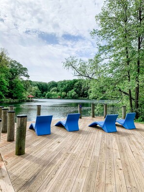 A wooden deck with blue lounge chairs overlooking a lake, surrounded by trees.