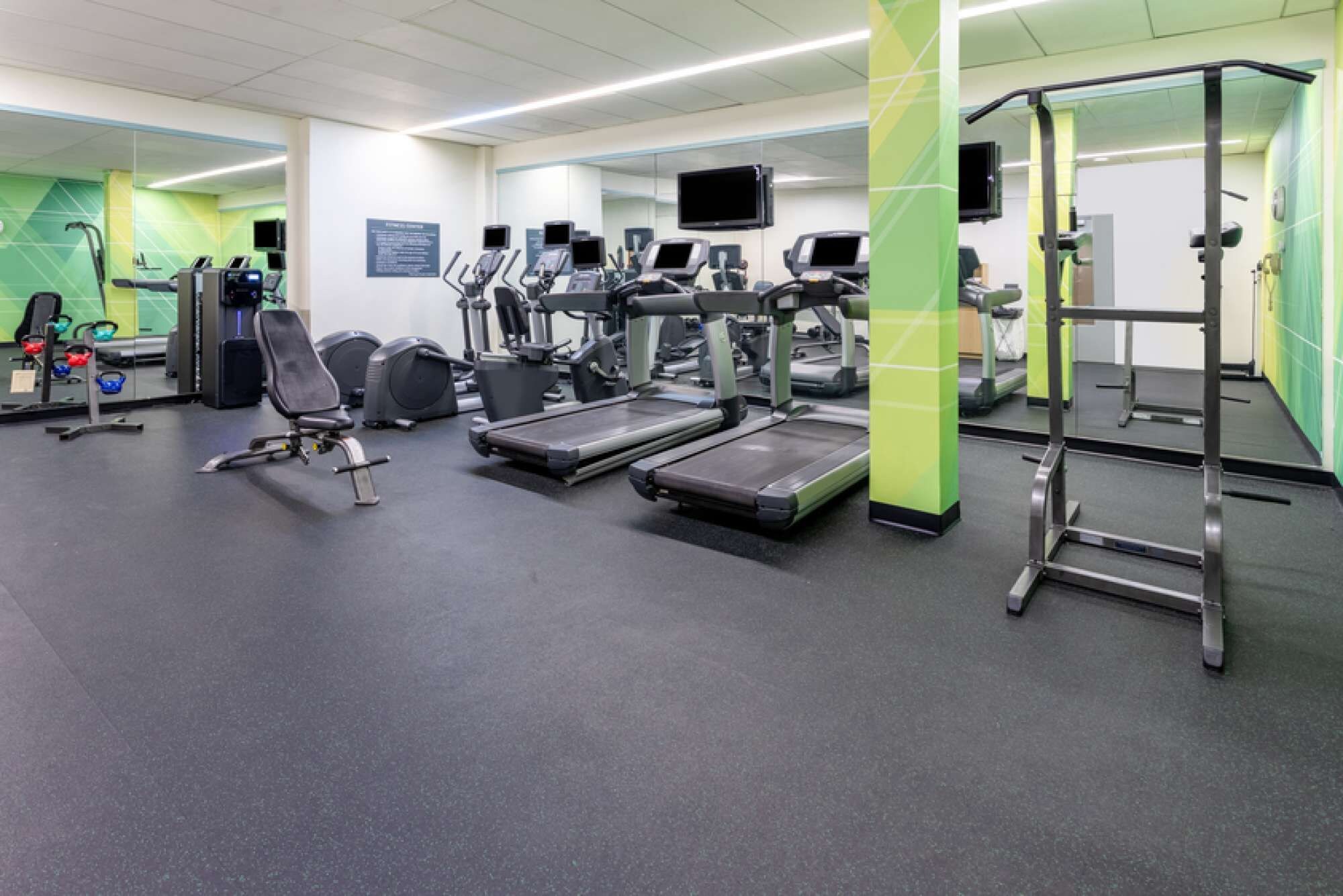 Un gimnasio con cintas de correr, elípticas y equipo de levantamiento de pesas.