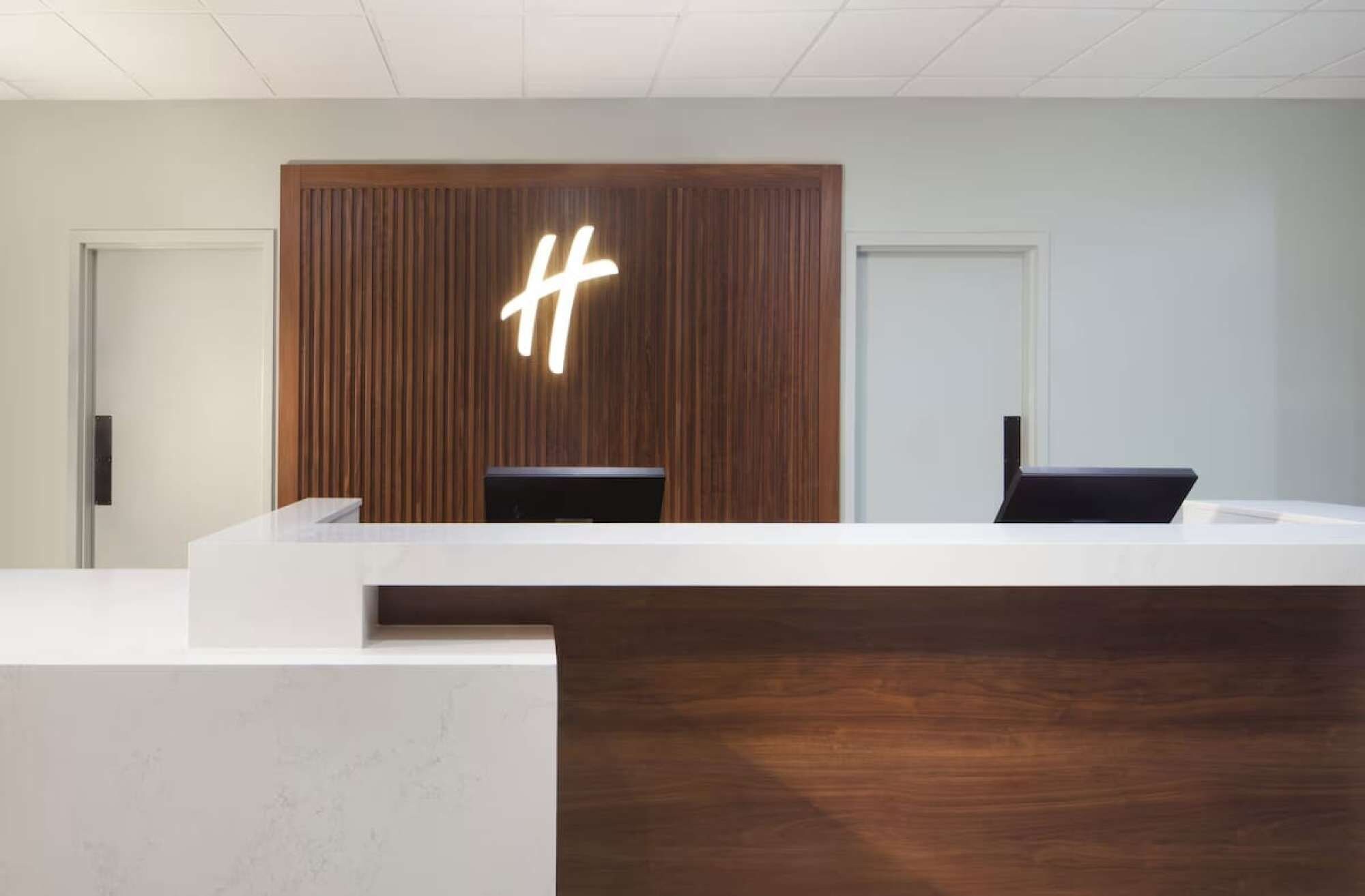 Un mostrador de recepción con paneles de madera y un gran letrero iluminado con la letra 'H'.