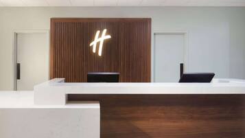 Un mostrador de recepción con paneles de madera y un gran letrero iluminado con la letra 'H'.