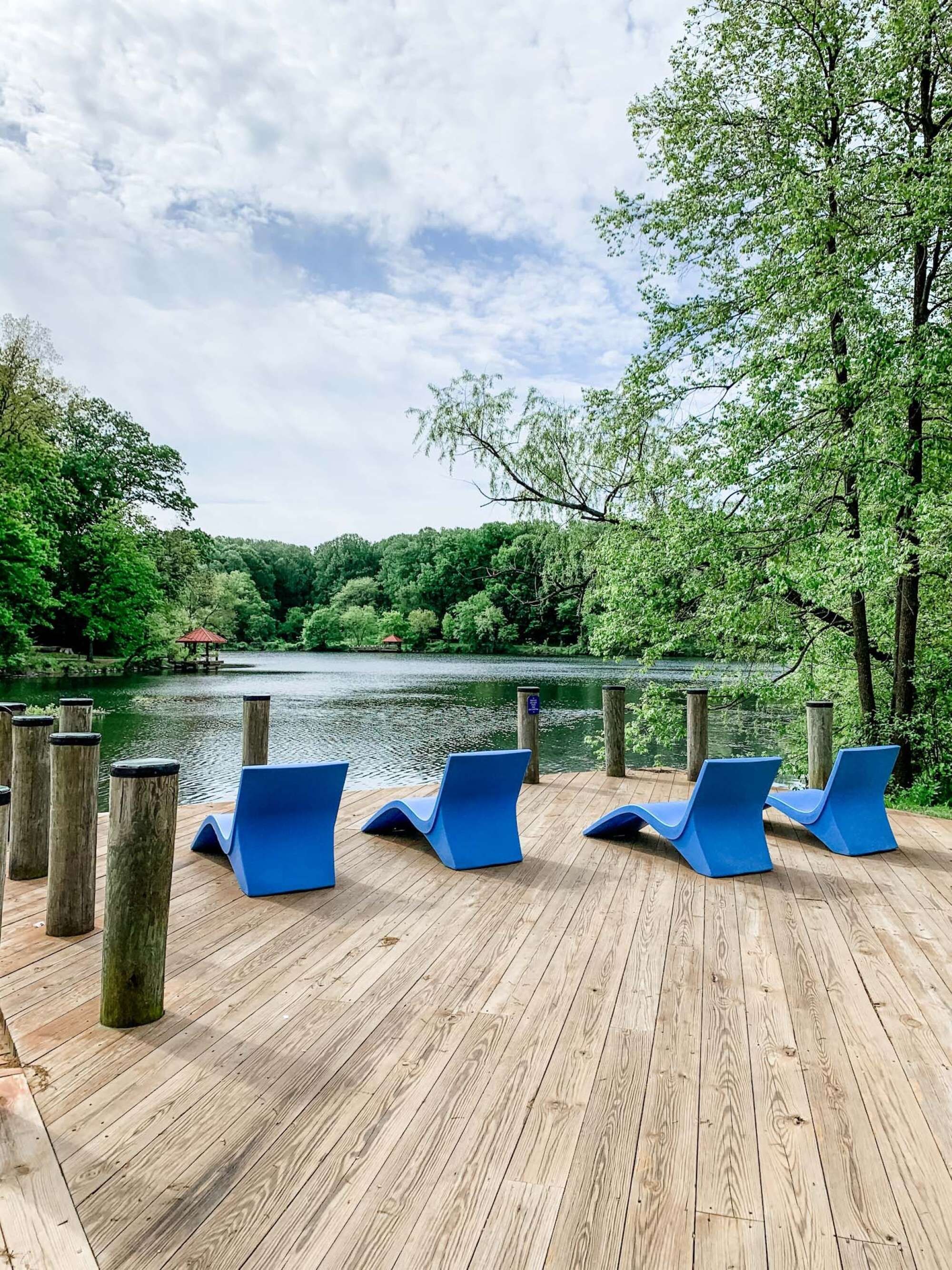 A wooden deck with blue lounge chairs overlooking a lake, surrounded by trees.
