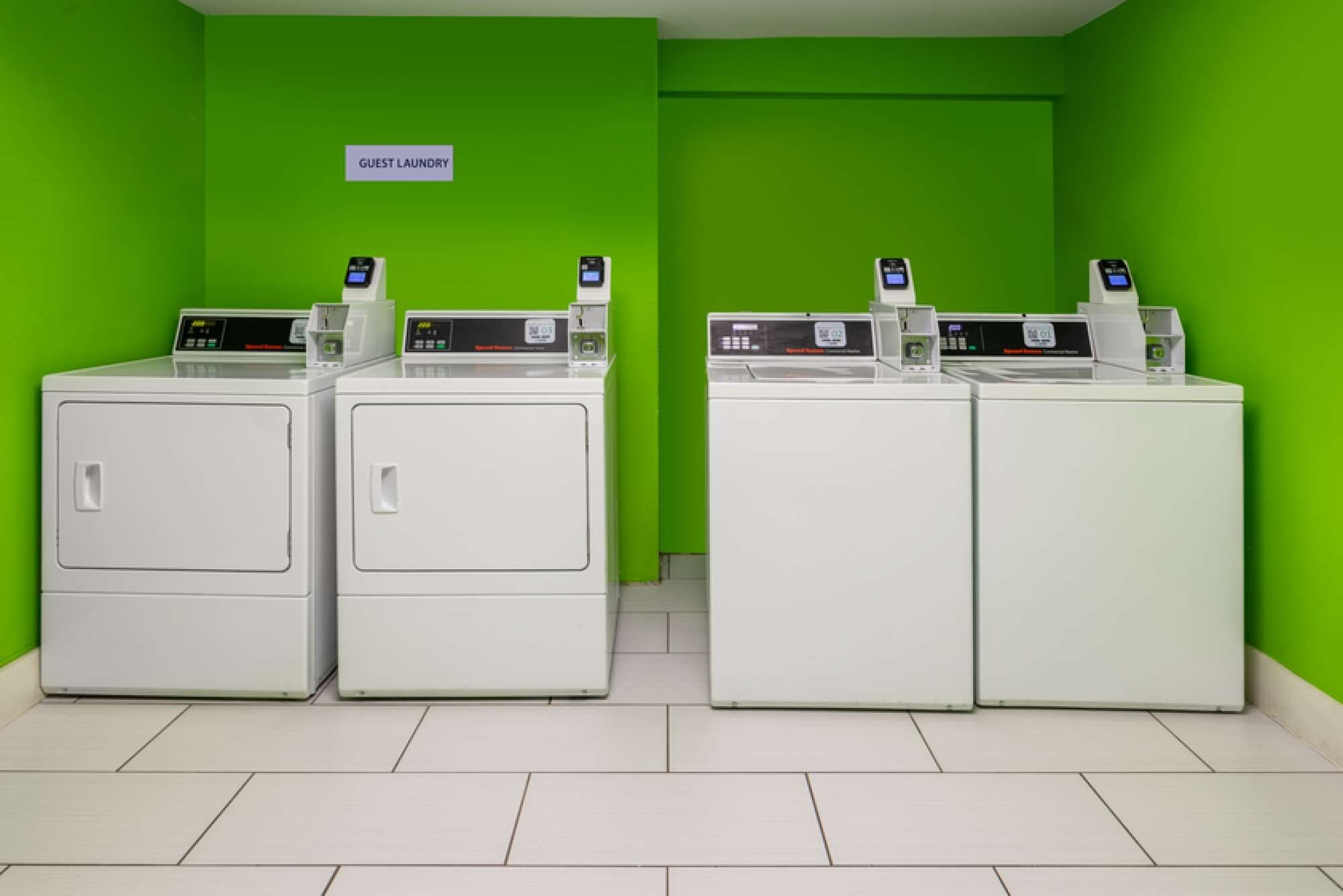 A laundry area with three washing machines and a sign indicating it's for guests.