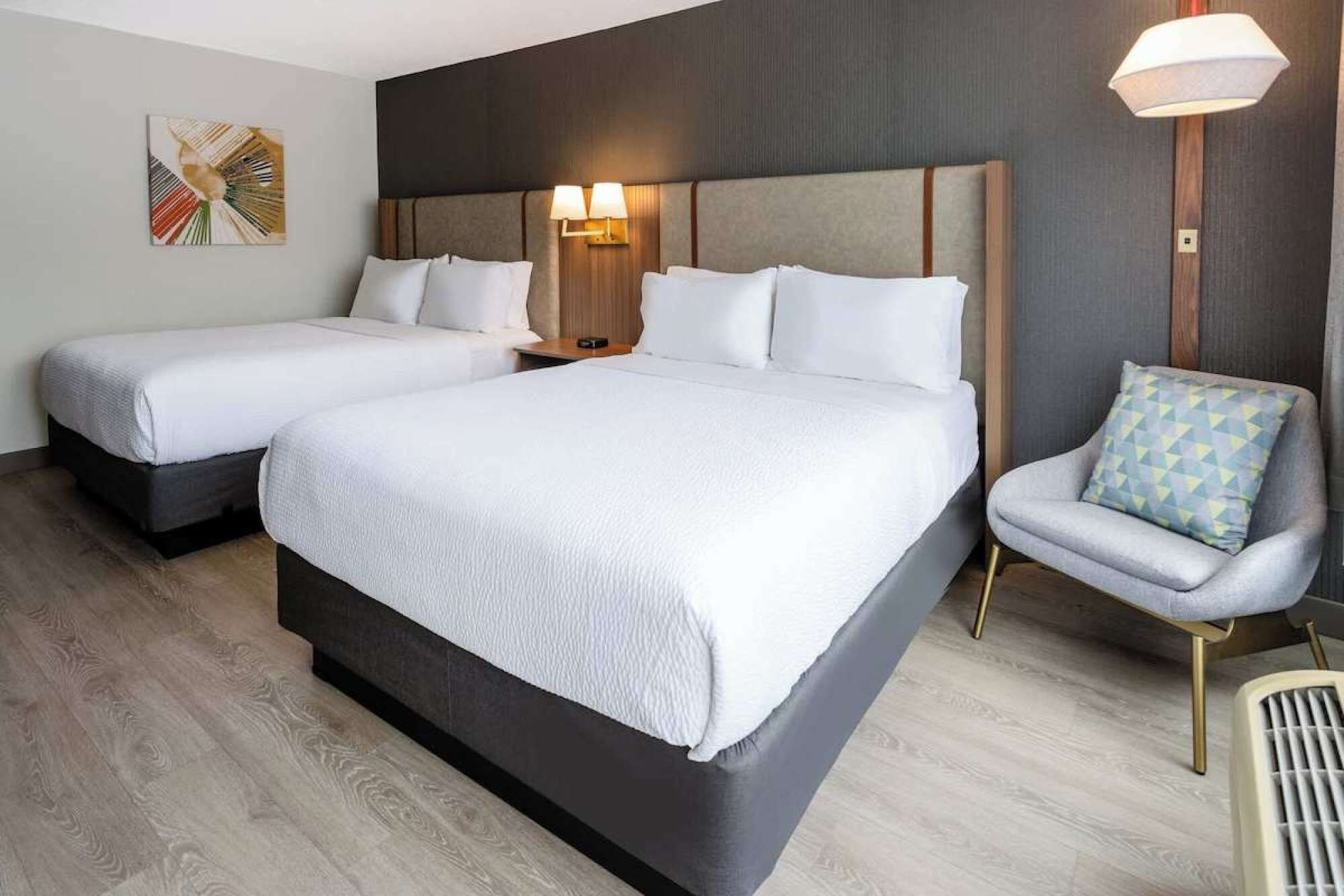 Una habitación de hotel con dos camas, una silla y una lámpara en la pared.