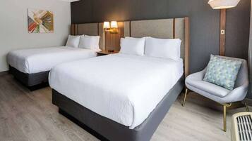 Una habitación de hotel con dos camas, una silla y una lámpara en la pared.