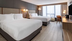 Et hotelværelse med to senge, et skrivebord, en stol og et fjernsyn.