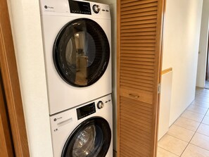Eine Waschmaschine und ein Trockner in einem Gerät mit Bedienfeld, platziert in einem Flur mit Holztür und gefliestem Boden.
