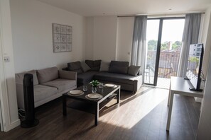 A modern living room with a sectional sofa, a coffee table, and a dining table. - Spacious Woolwich Apartment With sea View (London)