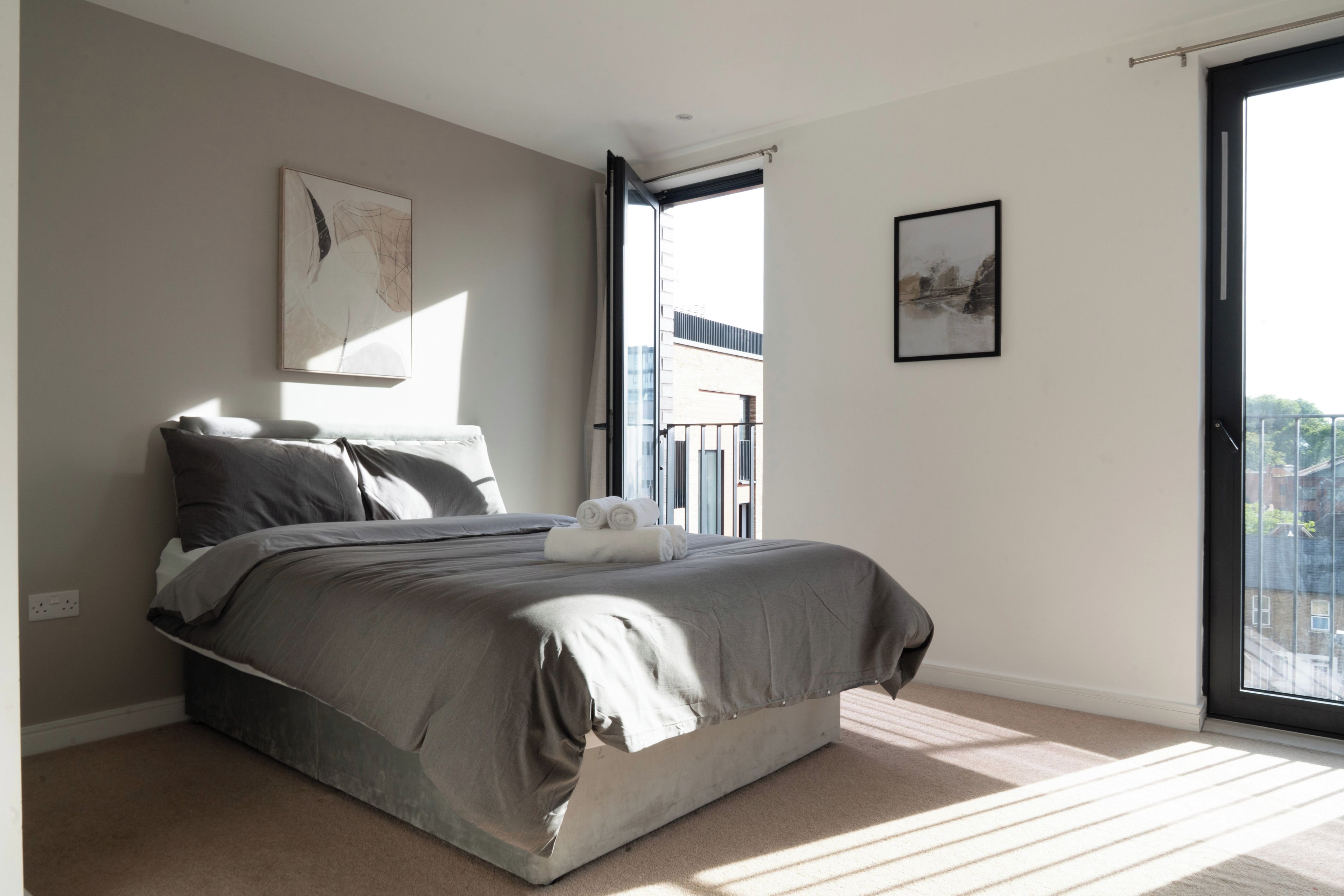 A modern bedroom with a large bed, a window with a view, and a door leading to a balcony.