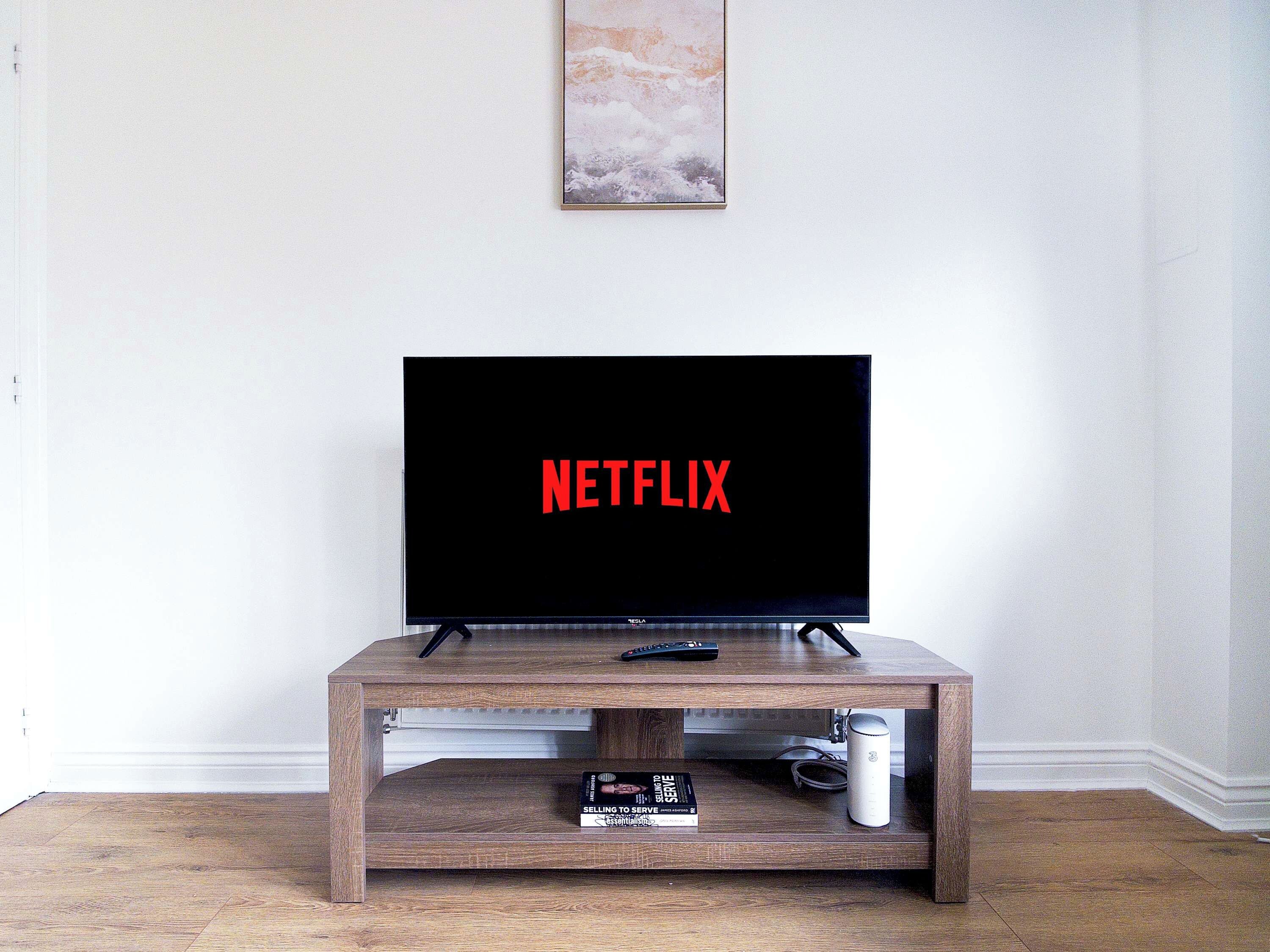 A television on a wooden stand with a remote control and a book titled 'Selling to Serve' on it.