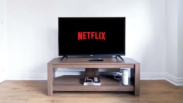 A television on a wooden stand with a remote control and a book titled 'Selling to Serve' on it.