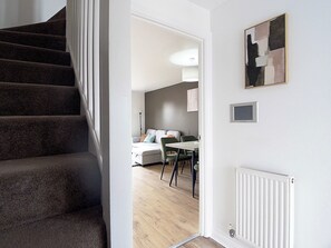 Een trap die leidt naar een kamer met een eethoek, een radiator en een ingelijste afbeelding aan de muur.