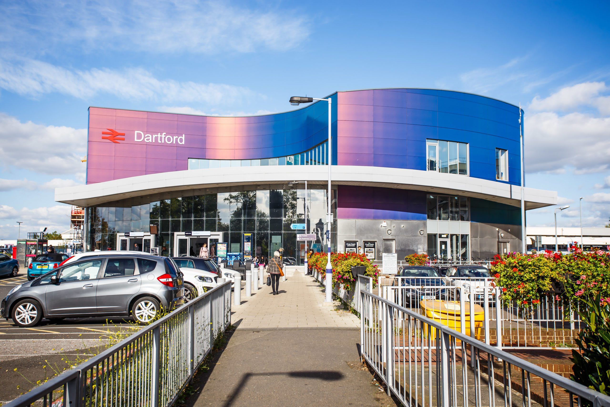Un bâtiment moderne à la façade incurvée, sur lequel on peut lire en grandes lettres le nom « Dartford », et une zone de stationnement avec des voitures et un passage piétonnier.
