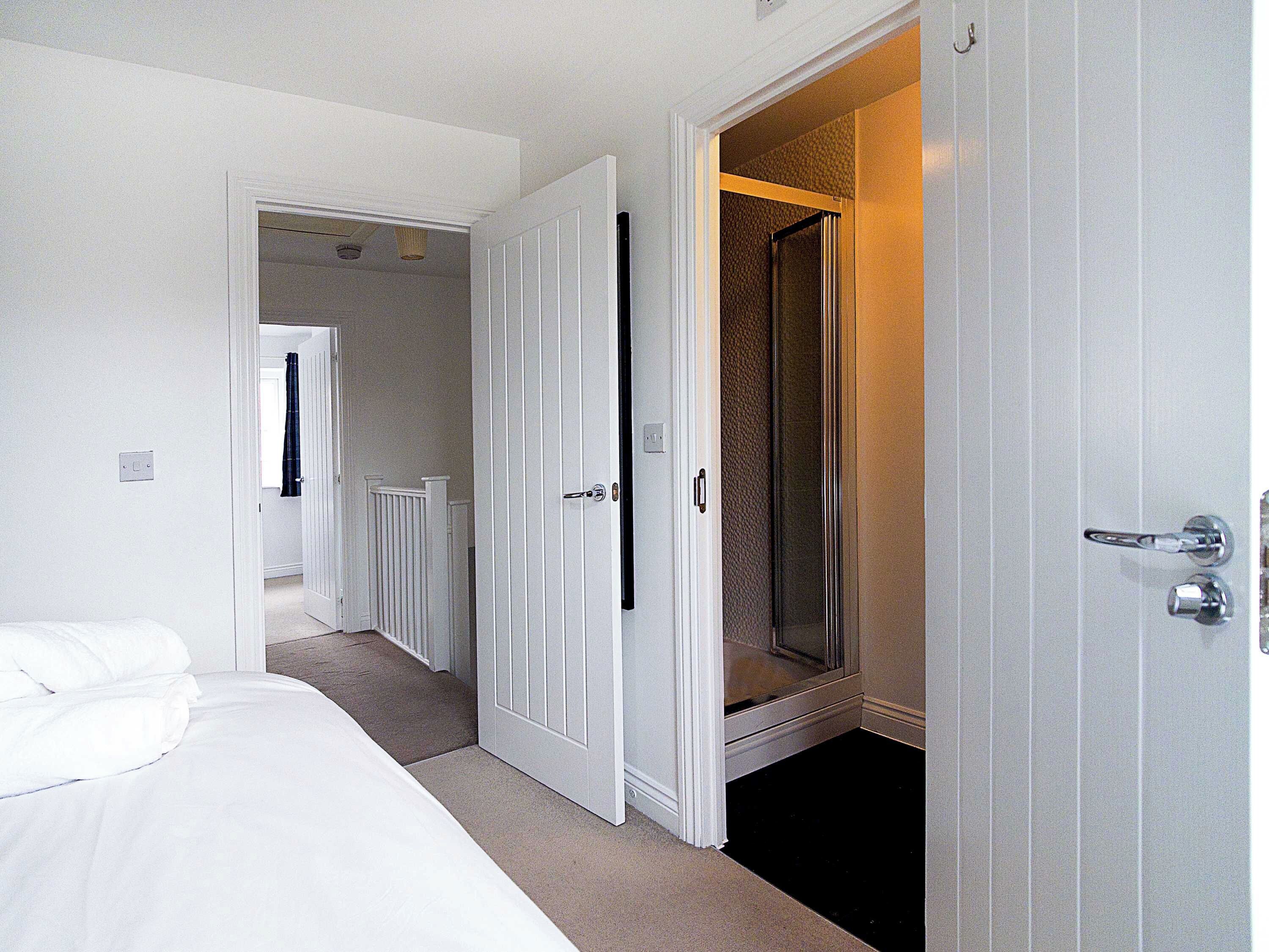 Habitación de hotel con cama, baño con ducha y pasillo que conduce a otra habitación.
